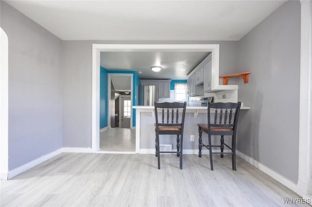 kitchen with kitchen peninsula, a kitchen breakfast bar, light hardwood / wood-style floors, and appliances with stainless steel finishes