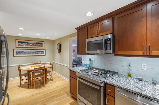 kitchen featuring light stone counters, light wood-type flooring, backsplash, and appliances with stainless steel finishes