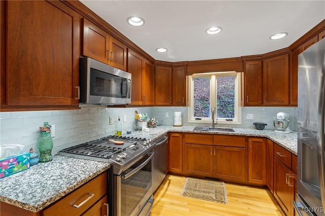 kitchen featuring light stone counters, sink, stainless steel appliances, and light hardwood / wood-style floors