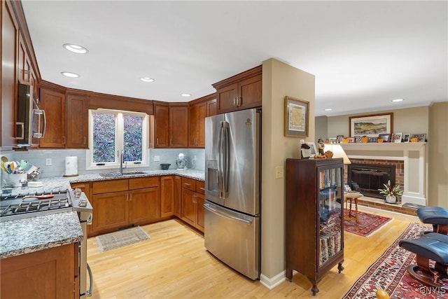 kitchen featuring light stone countertops, appliances with stainless steel finishes, a brick fireplace, sink, and light hardwood / wood-style flooring