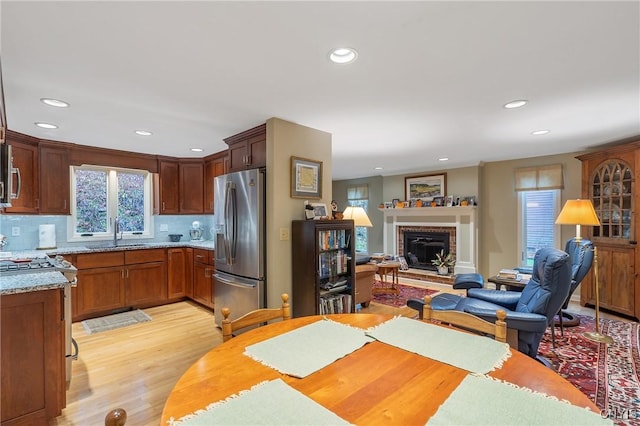 kitchen with appliances with stainless steel finishes, backsplash, light hardwood / wood-style flooring, and a brick fireplace