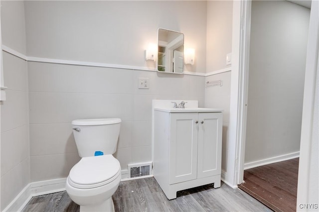 bathroom featuring vanity, toilet, wood-type flooring, and tile walls