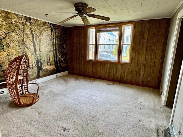 interior space featuring ceiling fan, light colored carpet, crown molding, and wooden walls