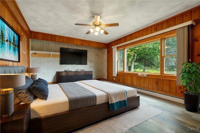 bedroom featuring ceiling fan, brick wall, a baseboard heating unit, wood walls, and hardwood / wood-style floors