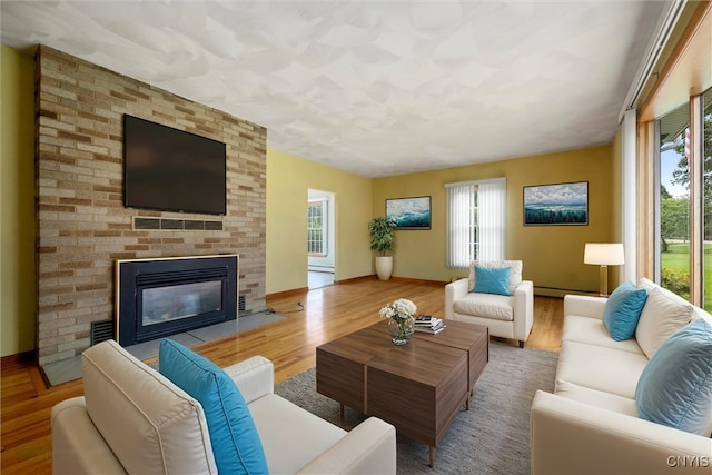 living room with wood-type flooring, a brick fireplace, and a baseboard heating unit