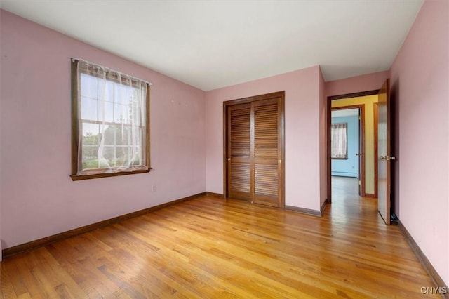 unfurnished bedroom with light wood-type flooring, baseboard heating, and a closet