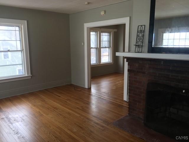 unfurnished living room featuring plenty of natural light, wood-type flooring, and a brick fireplace