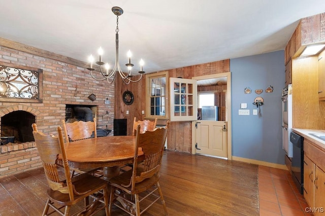 dining space featuring a brick fireplace, wood walls, dark wood-type flooring, and a chandelier