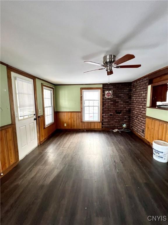 unfurnished living room with a wealth of natural light, dark hardwood / wood-style flooring, ceiling fan, and brick wall