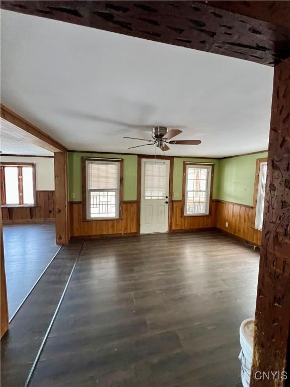 unfurnished living room featuring dark hardwood / wood-style floors, plenty of natural light, wooden walls, and ceiling fan