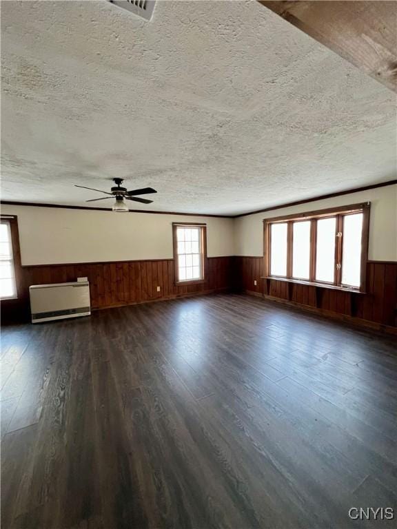 empty room with a textured ceiling, wood walls, ceiling fan, and dark hardwood / wood-style floors