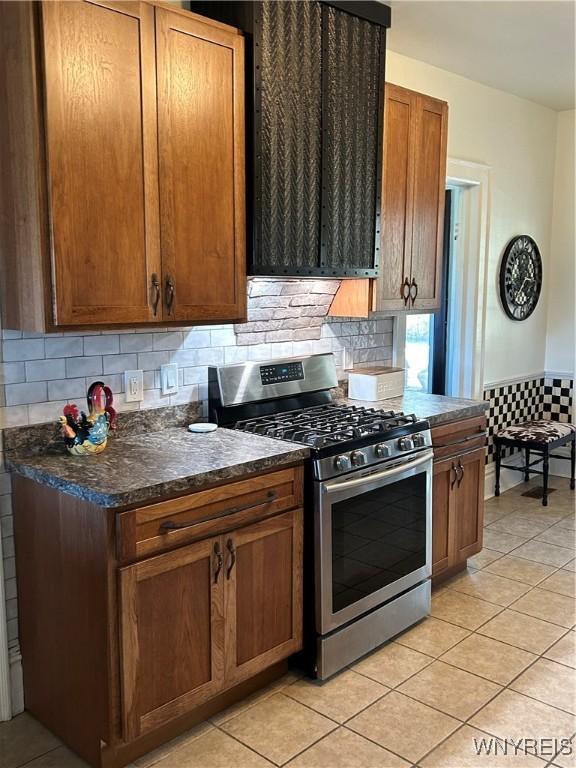 kitchen with light tile patterned floors, decorative backsplash, range hood, and stainless steel range with gas stovetop