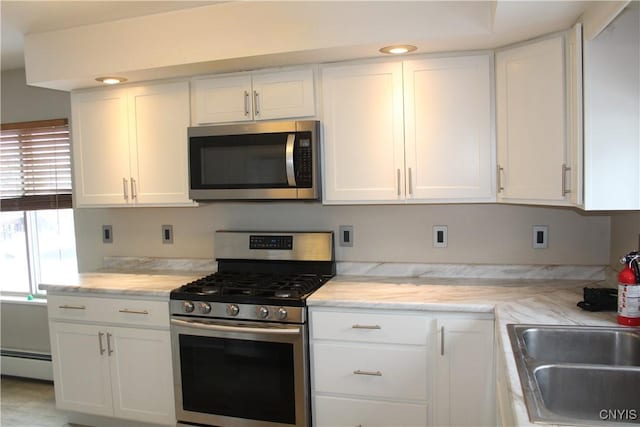 kitchen featuring appliances with stainless steel finishes, white cabinetry, baseboard heating, and sink