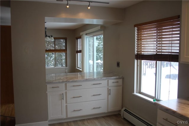 interior space with baseboard heating, white cabinetry, and a healthy amount of sunlight