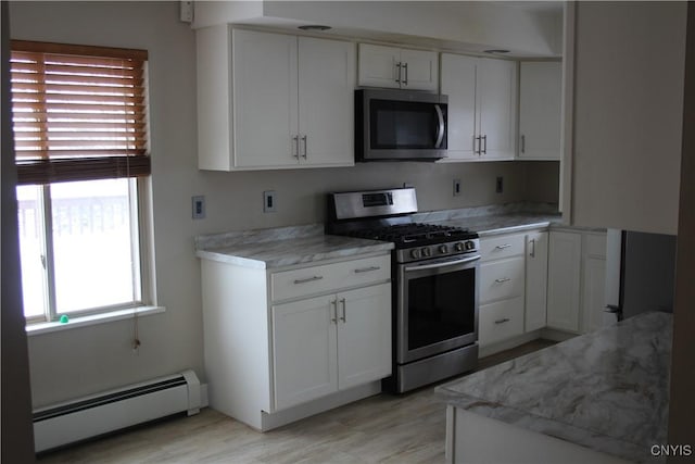 kitchen with appliances with stainless steel finishes, white cabinetry, baseboard heating, and plenty of natural light