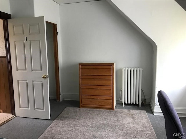 interior space with dark colored carpet, vaulted ceiling, and radiator