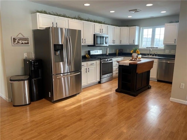 kitchen featuring appliances with stainless steel finishes, sink, light hardwood / wood-style flooring, white cabinets, and a center island