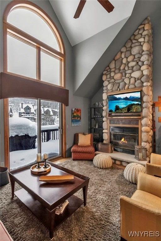 living room featuring a stone fireplace, ceiling fan, and high vaulted ceiling