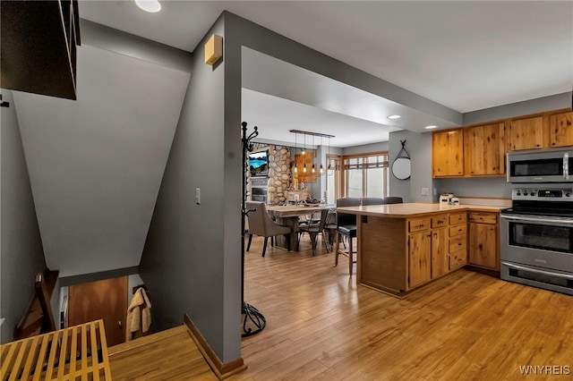 kitchen with decorative light fixtures, kitchen peninsula, appliances with stainless steel finishes, and light hardwood / wood-style flooring