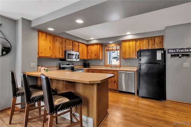 kitchen featuring sink, light hardwood / wood-style flooring, kitchen peninsula, a breakfast bar area, and appliances with stainless steel finishes