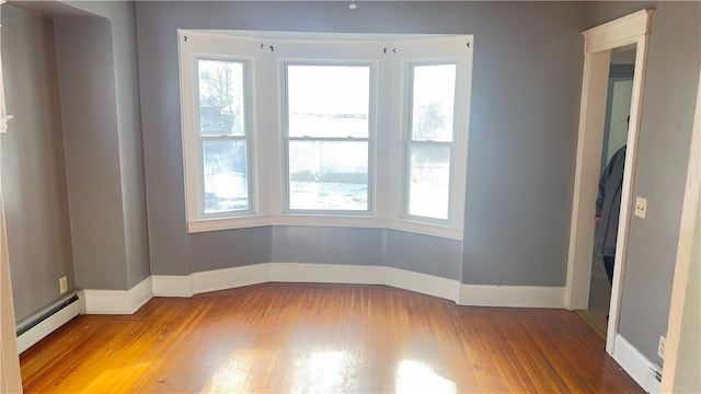 unfurnished room with baseboard heating, plenty of natural light, and hardwood / wood-style floors