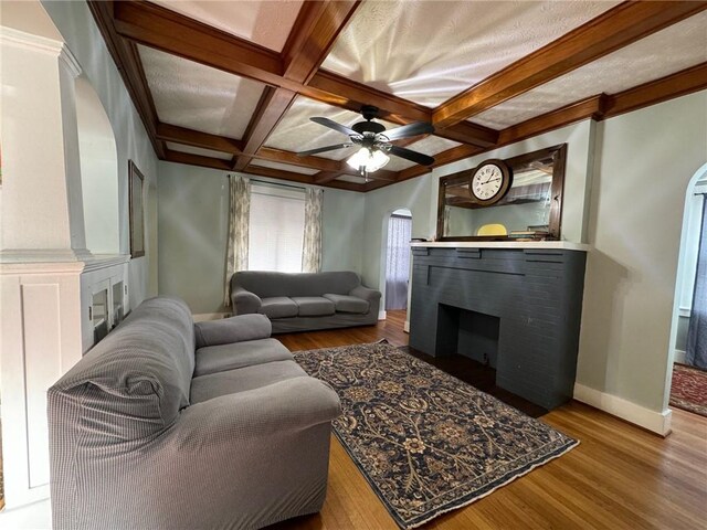 living room with ceiling fan, coffered ceiling, a brick fireplace, beamed ceiling, and hardwood / wood-style flooring