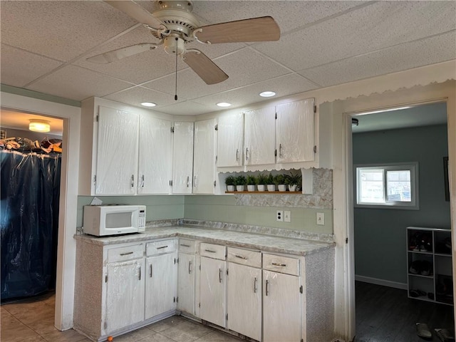 kitchen with a paneled ceiling, white cabinetry, light tile patterned floors, and ceiling fan