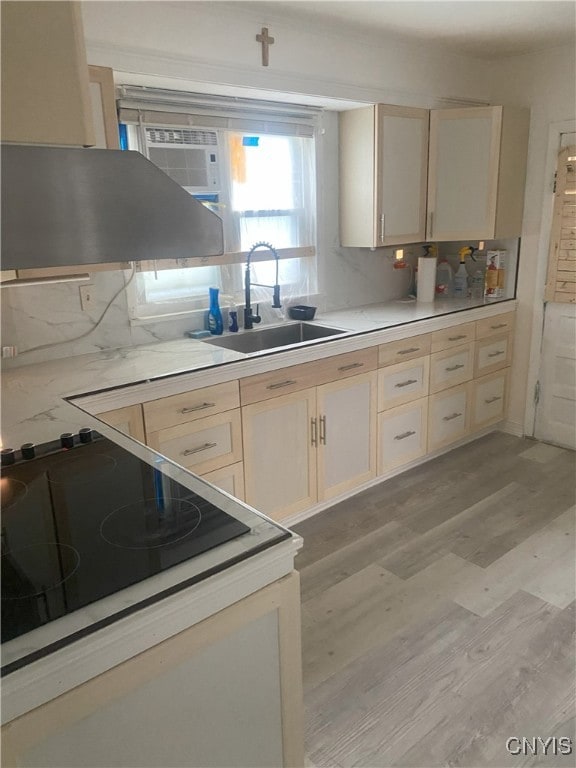 kitchen with black stove, sink, tasteful backsplash, exhaust hood, and light wood-type flooring