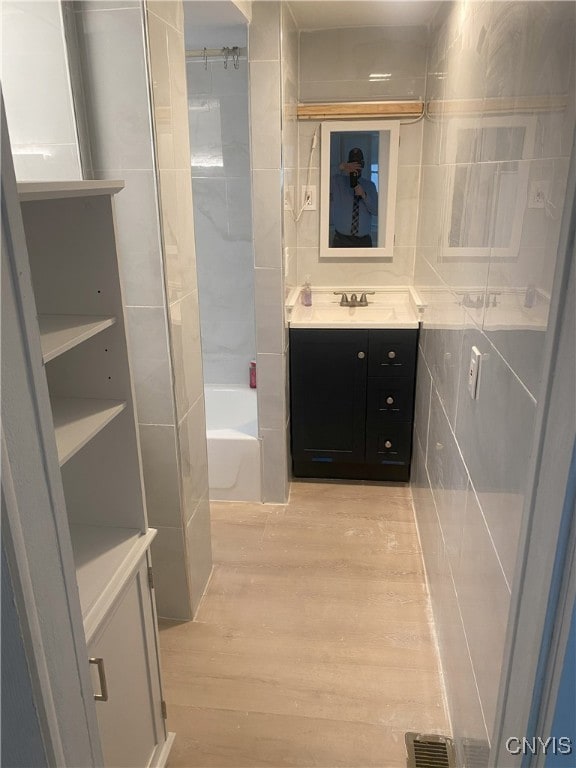 bathroom with hardwood / wood-style floors, vanity, shower / bathtub combination, and tile walls