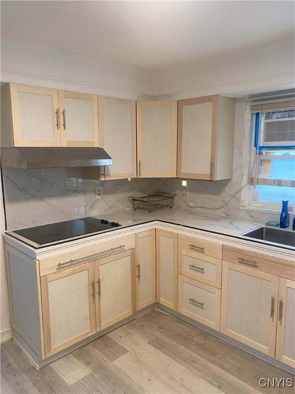 kitchen featuring black electric stovetop, light brown cabinets, light wood-type flooring, and backsplash