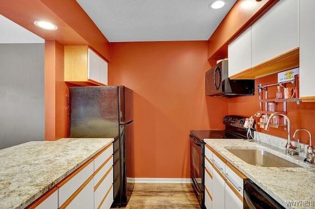 kitchen with light wood-type flooring, light stone counters, sink, black appliances, and white cabinets