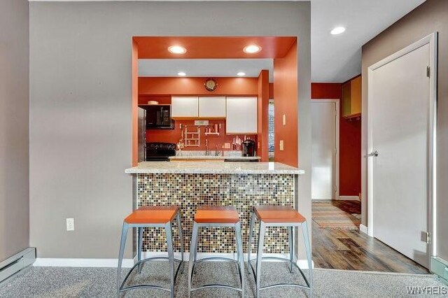 kitchen with backsplash, black appliances, hardwood / wood-style flooring, a baseboard radiator, and white cabinets