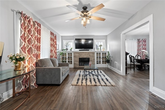 living room with a stone fireplace, ceiling fan, and dark wood-type flooring