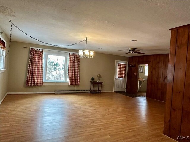 unfurnished room with ceiling fan with notable chandelier, a textured ceiling, wooden walls, a baseboard heating unit, and hardwood / wood-style floors