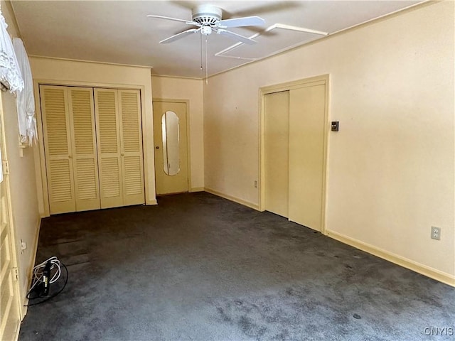 unfurnished bedroom with ceiling fan, dark carpet, and two closets