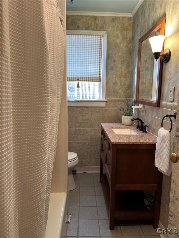 bathroom featuring tile patterned flooring, crown molding, toilet, vanity, and tile walls