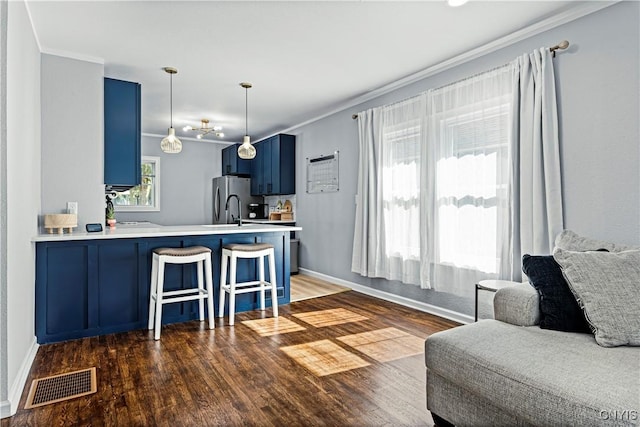 kitchen featuring kitchen peninsula, ornamental molding, a breakfast bar, blue cabinets, and dark hardwood / wood-style floors