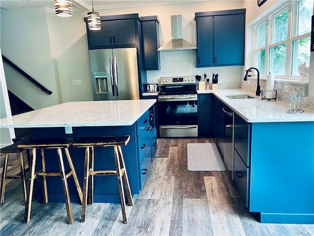 kitchen with wall chimney exhaust hood, a kitchen island, blue cabinets, and stainless steel appliances