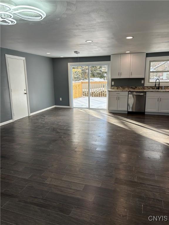 unfurnished living room featuring baseboards, a healthy amount of sunlight, dark wood-style flooring, and a sink
