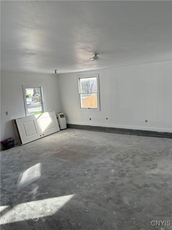 unfurnished room with a wealth of natural light, unfinished concrete floors, and baseboards