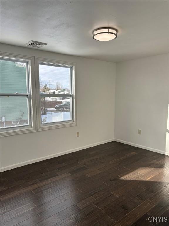 empty room with dark wood finished floors, visible vents, and baseboards