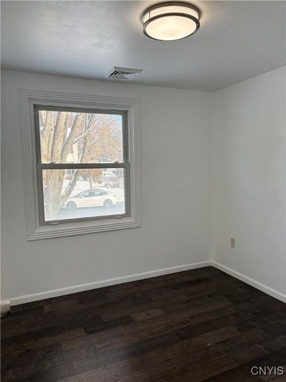 empty room featuring dark wood finished floors, visible vents, and baseboards