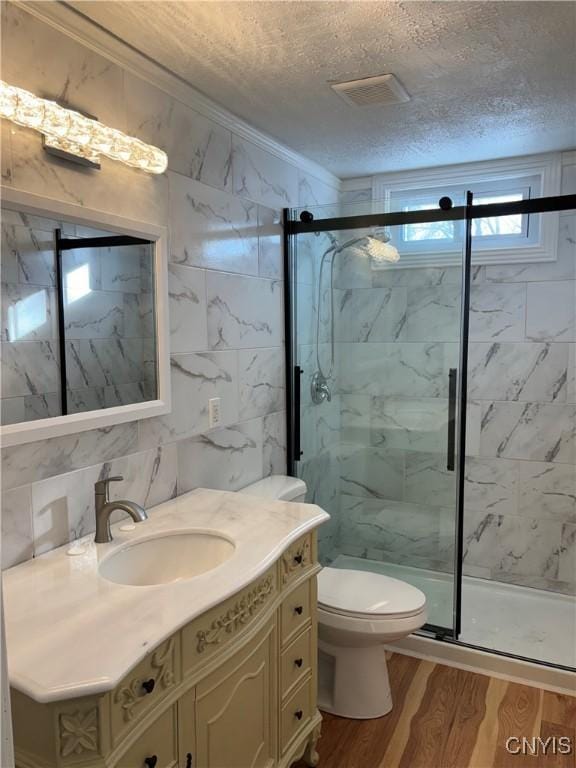 full bathroom featuring a textured ceiling, visible vents, a marble finish shower, ornamental molding, and wood finished floors