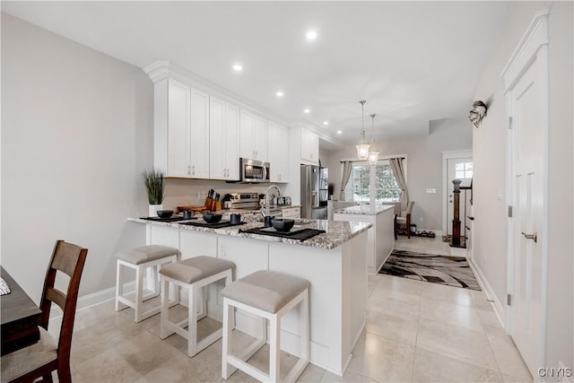 kitchen with hanging light fixtures, appliances with stainless steel finishes, kitchen peninsula, light stone countertops, and white cabinets