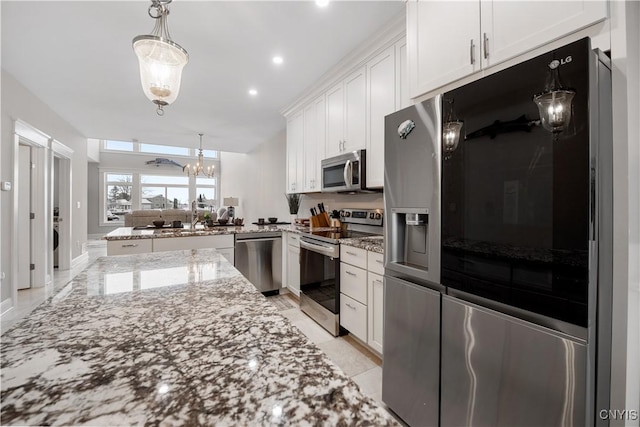 kitchen featuring white cabinetry, kitchen peninsula, pendant lighting, stainless steel appliances, and light stone countertops