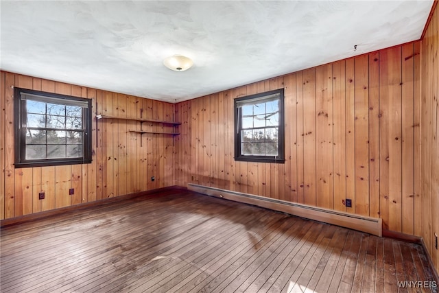 spare room with baseboard heating, a healthy amount of sunlight, wood-type flooring, and wood walls