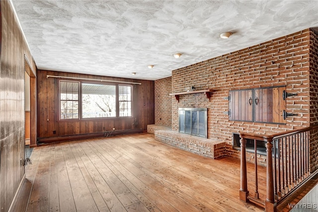 unfurnished living room featuring a textured ceiling, wooden walls, a baseboard radiator, light hardwood / wood-style flooring, and a fireplace