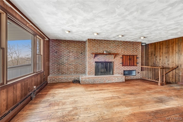 unfurnished living room featuring wood walls, a fireplace, brick wall, and hardwood / wood-style flooring