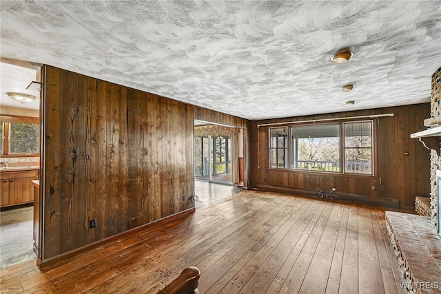 unfurnished living room with wood-type flooring, a stone fireplace, and wood walls