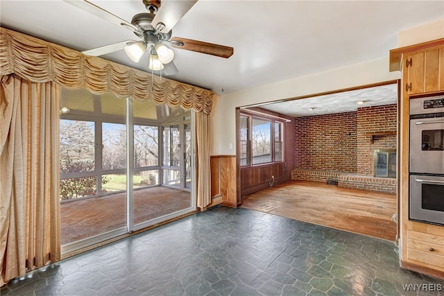 unfurnished living room with ceiling fan, brick wall, dark wood-type flooring, and a baseboard radiator